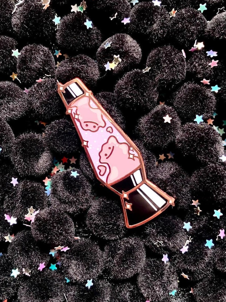 May include: A pink and black enamel pin shaped like a lava lamp with a glittery design and a smiling cloud inside.