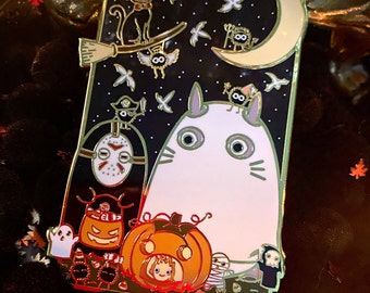 May include: A rectangular enamel pin with a gold border featuring a Halloween-themed design. The pin includes a white Totoro character, a black cat on a broom, a Jason Voorhees mask, a pumpkin, and other spooky characters against a starry night sky.