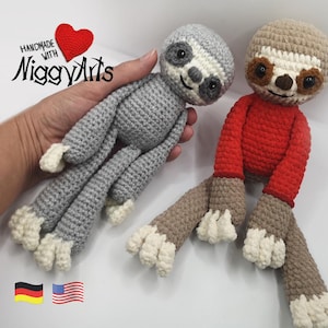 Könnte beinhalten: Zwei handgefertigte Häkelfaultiere. Eines ist grau mit weißen Akzenten, das andere ist braun mit einem roten Körper. Beide haben lächelnde Gesichter und lange Gliedmaßen. Der Text "Handmade with NiggyArts" ist sichtbar.