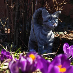 May include: A gray crocheted cat figurine with white accents, sitting in a bed of purple crocuses.