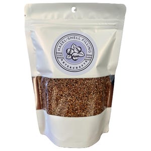 Könnte beinhalten: Ein weißer wiederverschließbarer Beutel gefüllt mit braunen Holzspänen. Der Beutel trägt ein Etikett mit der Aufschrift "Hazel-Shell Filling Arts & Crafts 120z 340g".