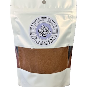 Puede incluir: Una bolsa blanca resellable con una etiqueta que dice "Hazel-Shell Powder Exfoliant 4 oz 114g" y un gráfico de una flor morada. La bolsa contiene un polvo marrón.