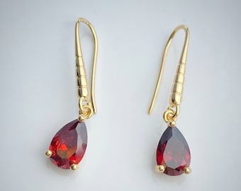 May include: A pair of gold dangle earrings with teardrop-shaped red gemstones.
