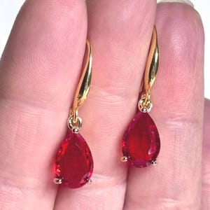 May include: A pair of gold teardrop earrings with red gemstone accents.