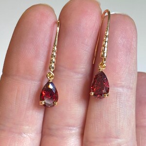 May include: A pair of gold dangle earrings with teardrop-shaped red gemstones.