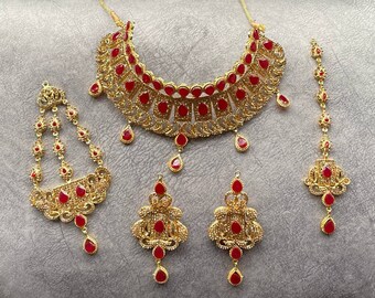 May include: A gold-tone bridal jewellery set with red stones. The set includes a necklace, earrings, and a tikka.