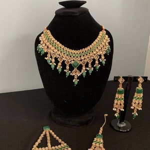 May include: A green and gold Indian bridal jewellery set with a necklace, earrings, and a maang tikka.