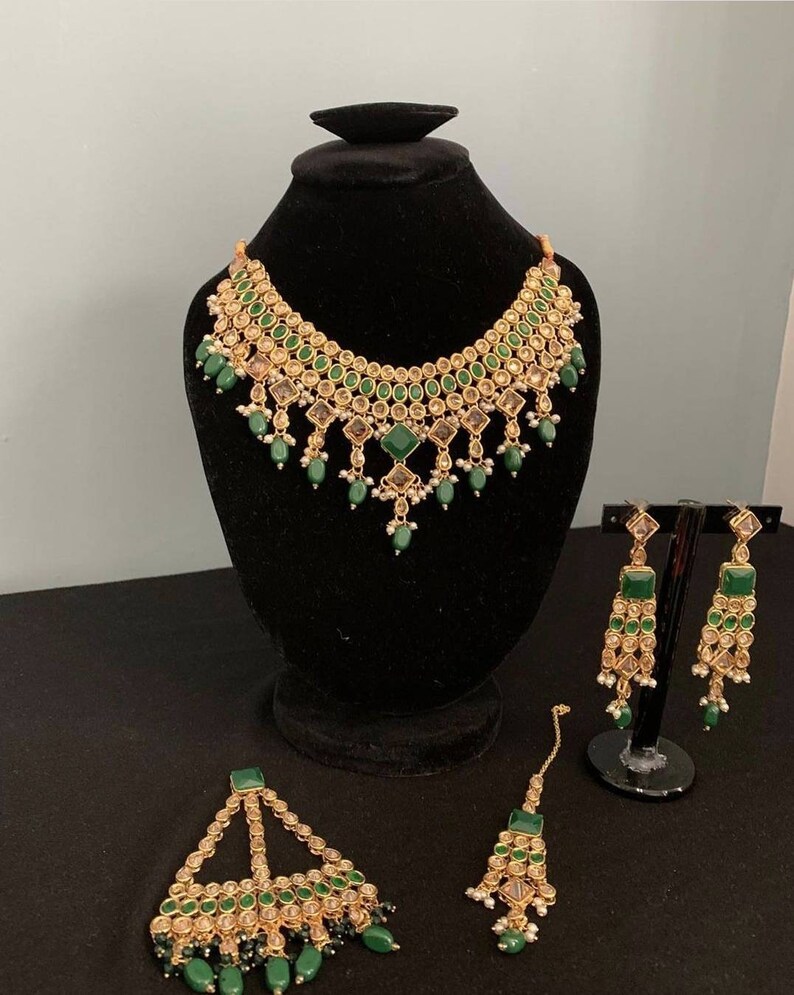 May include: A green and gold Indian bridal jewellery set with a necklace, earrings, and a maang tikka.
