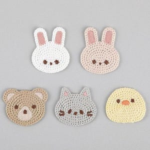 May include: Five crocheted animal coasters. The coasters are shaped like a bunny, a bear, a cat, a chick, and a bunny. The coasters are all different colours and have embroidered details.