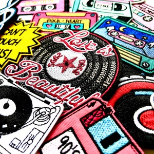 May include: A collection of colorful embroidered iron-on patches featuring music-themed designs, including cassette tapes, records, and the words "Love is Beautiful" and "80s Funk".