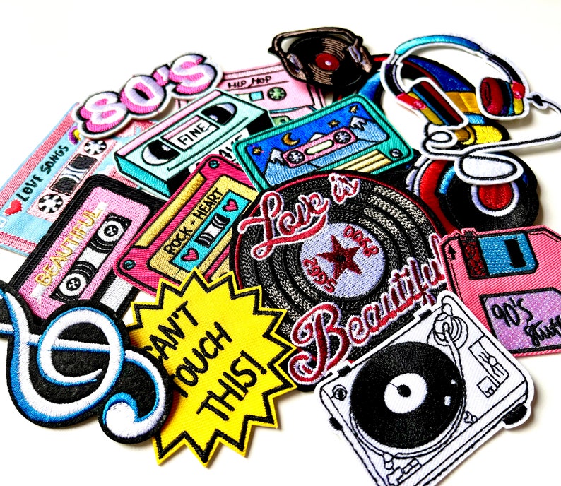 May include: A collection of colorful embroidered iron-on patches featuring retro music themes, including cassette tapes, turntables, a record, a music note, and headphones. The patches have text that reads "80's", "Love Songs", "Fine", "Hip Hop", "Rock Heart", "Love is Beautiful", "Can't Touch This!" and "90's Music".