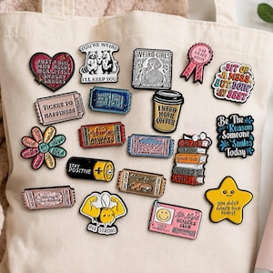Peut inclure: Une collection de pin's en émail aux motifs variés, incluant un cœur avec du texte, une tasse de café, une pile, une pile de livres, une abeille et plusieurs pin's en forme de ticket avec des phrases comme Ticket to Happiness et Always Anxious.