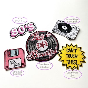 May include: A set of iron-on patches featuring 80's and 90's themed designs. The patches include a pink 80's logo, a black and white vinyl record with the text "Love is Beautiful", a pink floppy disk with the text "90's Stuff", a black and white record player, and a yellow starburst with the text "Can't Touch This!"