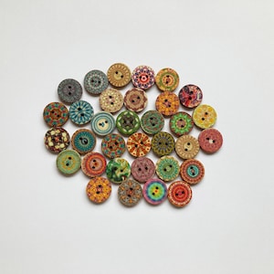Könnte beinhalten: Sortiment an bunten Holz-Knöpfen mit komplizierten Mandala-Designs. Die Knöpfe sind rund und haben zwei Löcher.