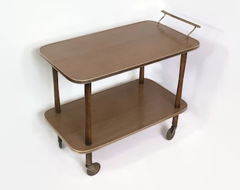 May include: A two-tiered wooden serving cart with a brass handle. The cart has a brown wood finish and four wheels.
