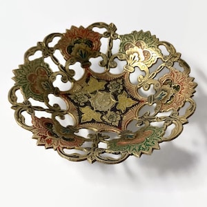 Può includere: Una piccola ciotola in ottone decorata con un design decorativo tagliato. La ciotola è dipinta con accenti rossi, verdi e dorati.