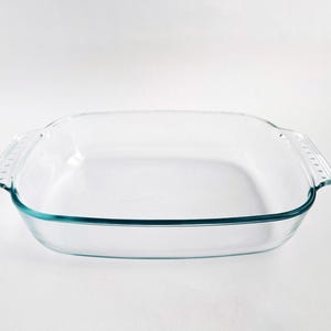 Puede incluir: Una fuente de horno cuadrada de vidrio transparente con un borde ligeramente redondeado y dos asas. La fuente tiene un tinte azul claro alrededor de los bordes y está diseñada para uso en horno. Ideal para hornear.