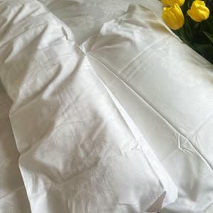 May include: Two white pillowcases with a subtle embossed pattern. The pillowcases are folded and arranged on a white surface.