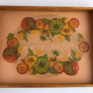 Könnte beinhalten: Ein Holztablett mit handbemaltem Design aus Kürbissen, Kürbissen und Blättern in Orange-, Grün- und Gelbtönen. Das Tablett hat ein abgenutztes, rustikales Aussehen.
