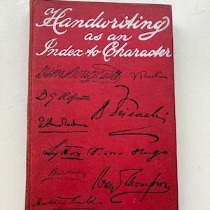 May include: Red book with the title "Handwriting as an Index to Character" written in white cursive lettering. The book cover is signed by several people in black ink.