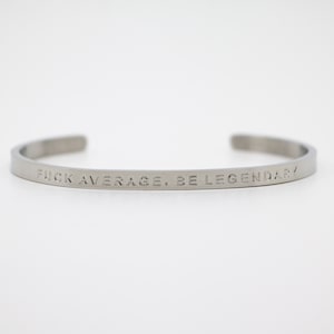 May include: A silver metal bracelet with the inscription "FUCK AVERAGE, BE LEGENDARY".