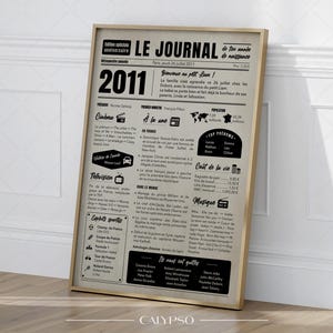 Peut inclure: Une impression encadrée d'un journal de 2011, avec des titres, des informations sur le cinéma, la télévision et le sport. L'impression a un fond beige avec du texte noir et s'intitule "LE JOURNAL". Le cadre est de couleur marron clair.