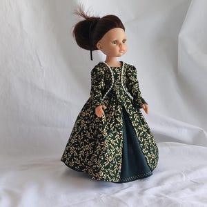 May include: A doll with brown hair styled in a bun, wearing a dark green dress featuring a gold leaf and vine pattern. The dress has long sleeves, a square neckline trimmed with white beads, and a solid dark green underskirt panel.