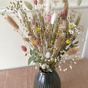 May include: A dried flower bouquet in a dark gray vase. The bouquet features a variety of dried grasses, flowers, and seed pods in shades of pink, white, yellow, and brown.