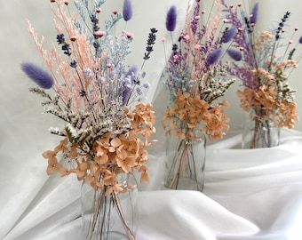 May include: Three glass vases filled with dried flowers in shades of pink, purple, and blue. The flowers include lavender, baby's breath, and hydrangeas.