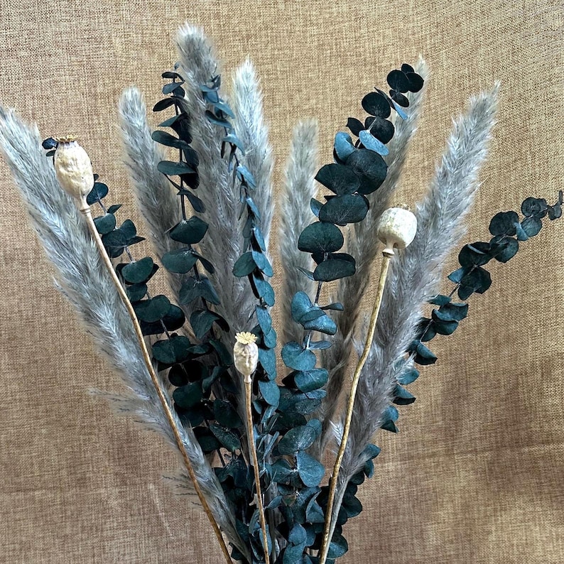 May include: A bouquet of dried pampas grass and eucalyptus stems with dried poppy seed pods. The pampas grass is a light beige color and the eucalyptus is a dark green color.
