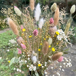 May include: A dried flower arrangement in a dark green vase. The bouquet features a variety of dried grasses, flowers, and seed pods in shades of white, pink, yellow, and brown.