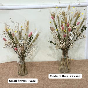 May include: Two glass vases filled with dried floral arrangements. The vase on the left is smaller and labeled "Small florals + vase". The vase on the right is larger and labeled "Medium florals + vase".