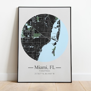 May include: A black and white map of Miami, Florida, with a light blue circle around the city. The map is framed in a black frame and has the text "Miami, FL - United States - 25.7617° N, 80.1918° W" below the map.