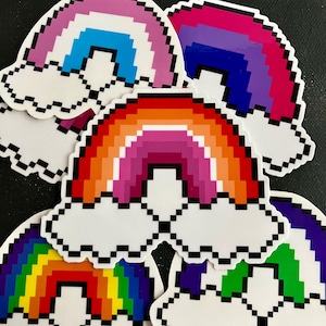 May include: A set of five rainbow pixel art stickers. Each sticker features a rainbow with clouds, in different color combinations. The rainbows are in a pixelated style, giving them a retro video game aesthetic.