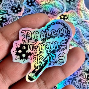 May include: A holographic sticker with a dripping black and white design. The sticker features a spiked ball, a chain, and the text "Protect Your Jams".