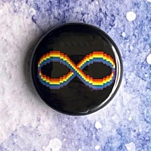 Può includere: Un bottone rotondo nero con un simbolo dell'infinito pixelato nei colori dell'arcobaleno. Il simbolo è centrato sul bottone, che ha una finitura lucida. Lo sfondo è un acquerello blu e bianco.