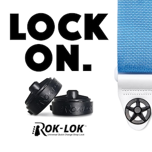 Op de afbeelding: Een close-up van een blauwe gitaarband met witte stiksels en een zwarte Rok-Lok snelwisselgitaarbandvergrendeling. De gitaarbandvergrendeling is een universeel ontwerp en wordt getoond bevestigd aan de band.