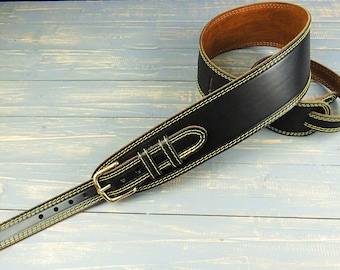 May include: A black leather guitar strap featuring bright yellow contrast stitching along the edges. The strap includes a brass-toned metal buckle for adjustment and a brown interior lining, designed with reinforced holes at both ends.
