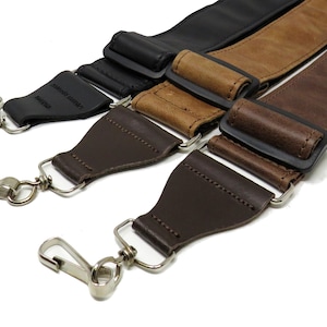 May include: Three leather camera straps with metal clasps. The straps are brown, tan, and black.