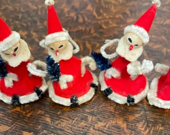 May include: Four vintage felt Christmas ornaments shaped like Santa Claus. Each ornament is red with white trim and a blue and white pom-pom. The ornaments have a white felt face with black eyes and a red nose.