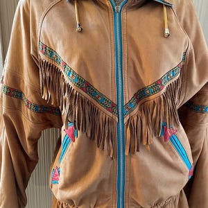 May include: A brown leather jacket with a blue zipper and fringe detail. The jacket has a geometric pattern in red, blue, and green.