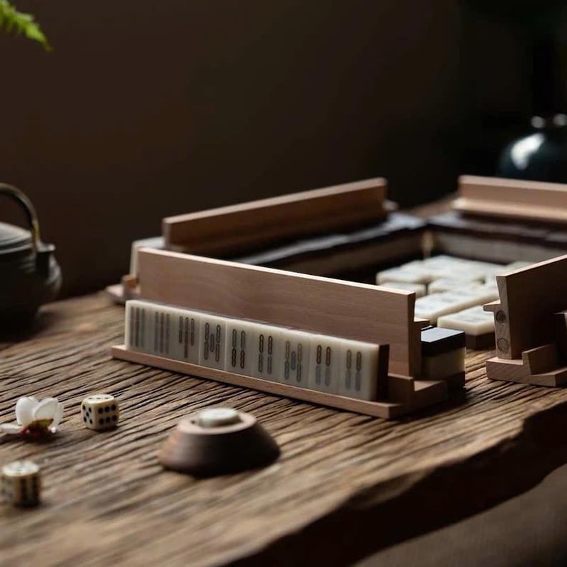 May include: A wooden mahjong set with white tiles and black markings. The tiles are arranged in a rectangular shape and are surrounded by a wooden frame. The set is on a wooden table.