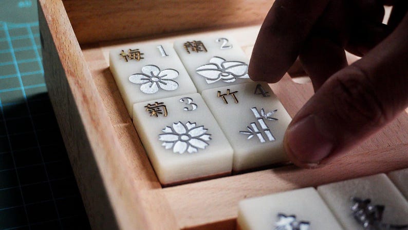 May include: A set of four white tiles with gold lettering and silver floral designs. The tiles are arranged in a square pattern and are sitting on a wooden surface. The tiles are numbered 1 through 4 and have the Chinese characters for "plum", "orchid", "bamboo", and "chrysanthemum".