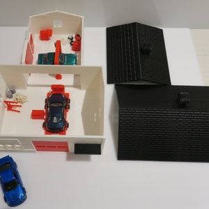 May include: A white toy garage with a red door and a blue car inside. There are two black roofs on the side.