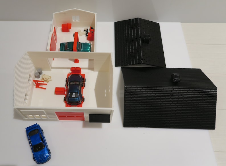 May include: A white toy garage with a red door and a blue car inside. There are two black roofs on the side.
