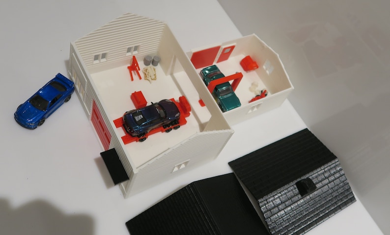 May include: A white toy garage with red doors and a blue car outside. Inside the garage are two toy cars, one blue and one green, on a red lift. There are also various tools and accessories inside the garage.