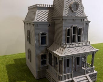 May include: A gray 3D printed model of a two-story house with a porch and a front door. The house has a gabled roof with a dormer window and a small round window in the roof.