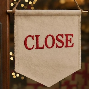 以下が含まれることがあります： 赤で刺繍された「CLOSE」の文字が入った、クリーム色のペナント型の看板。 看板は木のダボから吊り下げられ、天然の紐で吊り下げられています。 看板は木のドアに表示されています。
