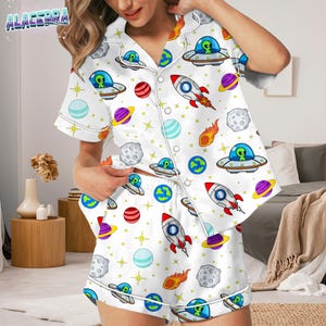 Puede incluir: Conjunto de pijama blanco con estampado espacial que presenta cohetes, planetas, ovnis y estrellas. La parte superior de manga corta y los pantalones cortos tienen ribetes blancos y una parte delantera abotonada. El conjunto de pijama est&aacute; hecho de un material suave y c&oacute;modo.