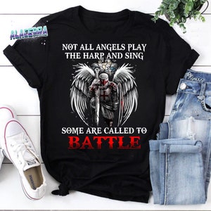 May include: Black t-shirt featuring a graphic of an angel warrior holding a sword and shield. The text "Not all angels play the harp and sing. Some are called to battle" is printed on the shirt.